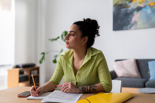 A contemplative woman holding a pencil over documents on a desk, planning her day in a bright room.