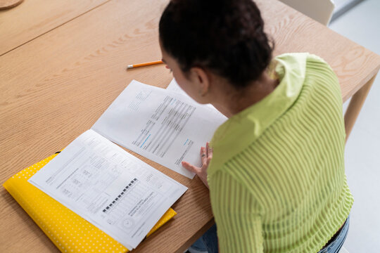 A woman engrossed in paperwork at a wooden table, with focus on the documents in a well-lit room.