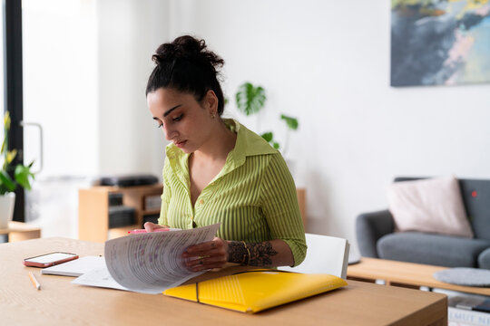 A woman engrossed in paperwork at a wooden table, with focus on the documents in a well-lit room.
