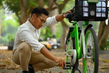 Attractive male office worker repairing his bike in the public park