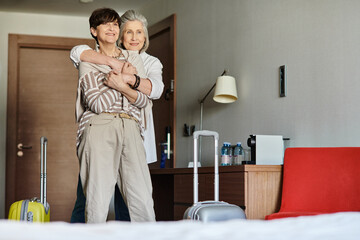 Fototapeta premium Senior lesbian couple share a tender hug in a luxurious hotel room.