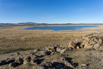 Huge stones on the foreground and lake with clear water. Mountains and agricultural fields. Bright blue sky