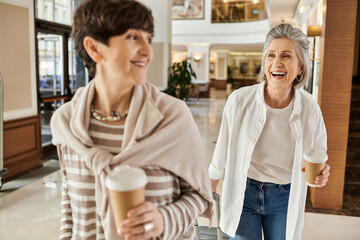 Two women enjoying a stroll through a mall while holding coffee cups.
