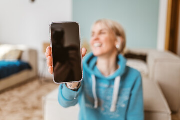 Joyful blonde woman holding smartphone towards camera with copy space