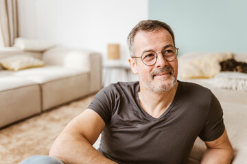 Contented Middle-Aged Man in Glasses Sitting on Living Room Floor with a Warm Smile