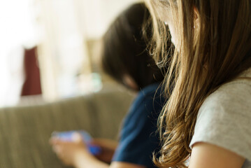 Mother and daughter using mobile phone sitting on sofa in living room at home