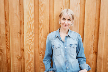 Blonde Woman in Denim Shirt Standing in Front of Wooden Wall Outdoors