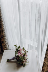 A bouquet of flowers sits on a table next to a window. The flowers are pink and green, and the arrangement is beautiful. The window lets in natural light, creating a warm and inviting atmosphere