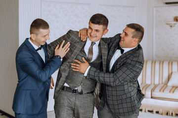 Three men in suits are hugging each other. One of them is wearing a tie. Scene is friendly and...