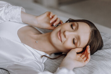 A woman is laying on a bed with her hands on her face. She is smiling and she is relaxed