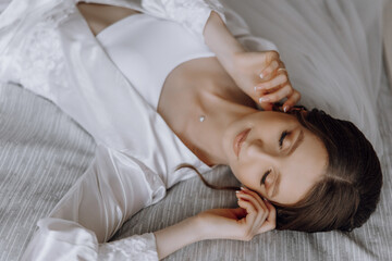 A woman is laying on a bed in a white robe. She is wearing a necklace and earrings