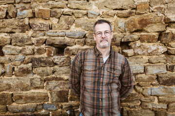 Confident Middle-aged Man in Checkered Shirt Posing in Front of Stone Wall