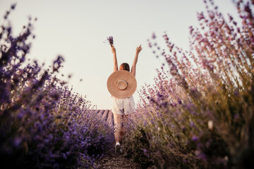 A woman is walking through a field of purple flowers with a straw hat on