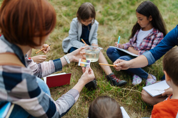 Young students analyzing water quality, ph level with indicator strips during biology field teaching class. Female teacher during outdoor active education.
