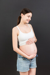 expecting mother in unzipped jeans showing her naked pregnant belly at colorful background with copy space. Pregnancy concept