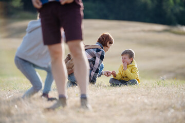 Teacher helping injured boy after fall. Young students running across meadow during field teaching...