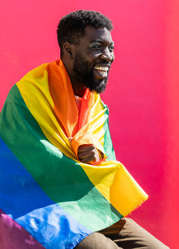 Happy non-binary person covered with colorful flag against pink background
