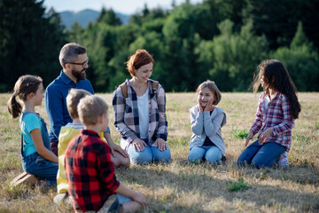 Children and teachers sitting on grass on meadow playing clapping game. Dedicated teachers during...