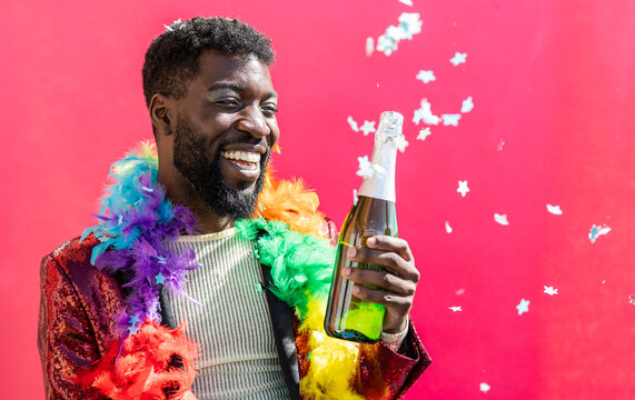 Cheerful non-binary person celebrating with champagne bottle against pink background