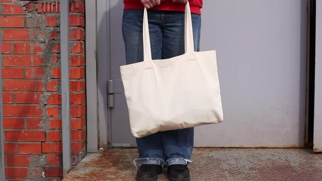 Woman in red hoodie holding tote canvas blank eco bag on street brick wall background. Female consumer hold white textile shopper. template or place for your design, logo, text