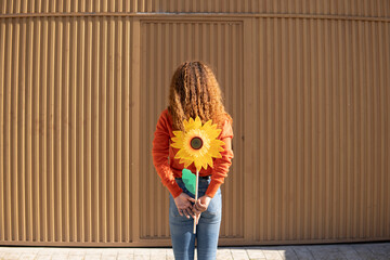 Young woman holding artificial sunflower in front of metal wall
