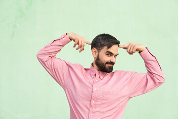 Smiling man touching head with fingers and dancing against mint green background