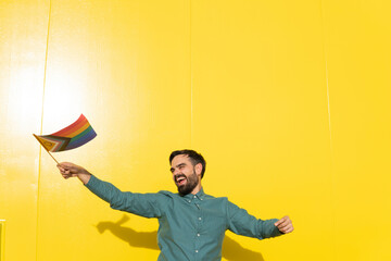 Happy man holding LGBTIQ pride flag in front of yellow wall
