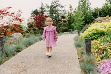 Little child girl in stylish dress walking in summer garden