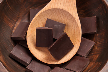 Fresh organic broken dark chocolate pieces in wooden rustic spoon close up. Sweet indulgence chunks