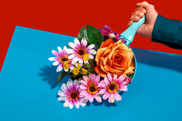 Hand of man holding frying pan with colorful flowers against colored background