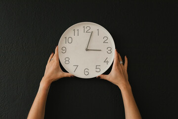 Hands of woman holding wall clock against black background