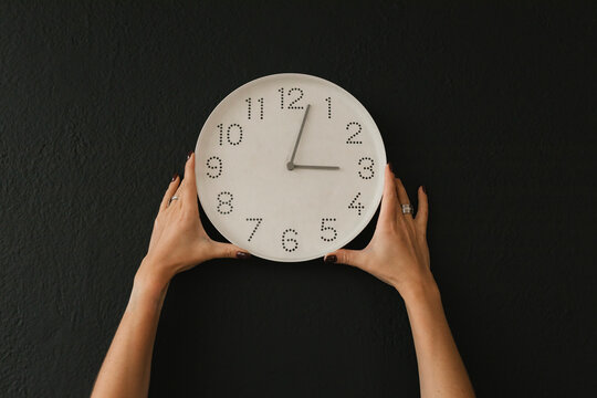 Hands of woman holding wall clock against black background