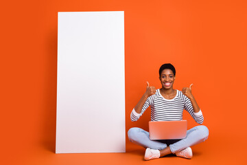 Portrait of attractive cheerful girl using laptop copy space showing thumbup isolated over vibrant orange color background