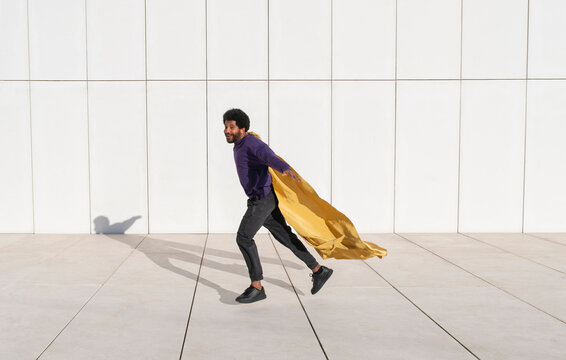 Playful man running in front of white wall wearing a cape