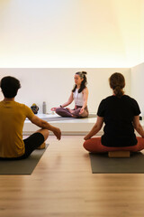 A group of people are sitting on yoga mats meditating in a room. One woman is teaching the others...