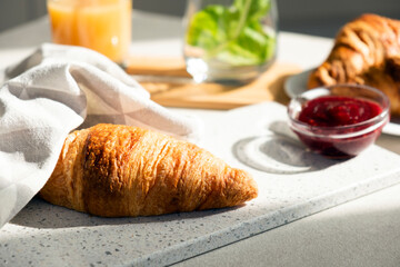 Fresh croissant for breakfast with jam on white board. Delicious celebratory breakfast in sunlight....