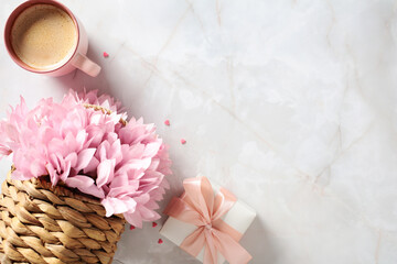 Happy Mothers Day concept. Wicker basket with pink flowers, coffee mug, gift box on stone table....