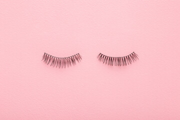 Dark black false lashes on light pink table background. Pastel color. Female beauty product. Closeup. Top down view. - 800102452