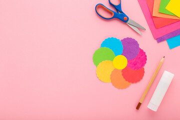 Colorful flower shape, scissors, glue stick, pencil and application paper on light pink table...