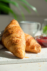 Fresh croissant for breakfast with cup of coffee on white board. Delicious celebratory breakfast in sunlight. Bakery or confectionery. Romantic morning meal.