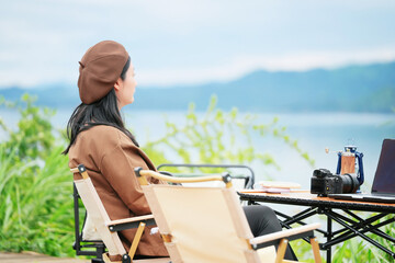 A woman is sitting on a chair and looking at the lake.