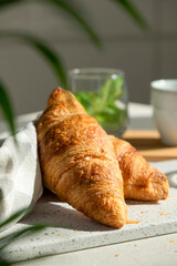 Fresh croissant for breakfast with cup of coffee on white board. Delicious celebratory breakfast in sunlight. Bakery or confectionery. Romantic morning meal.