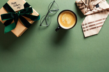 Happy Fathers Day flat lay composition with gift box, glasses, coffee cup, tie on dark green table.
