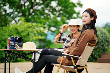 Two women relaxing in camping chairs in the woods