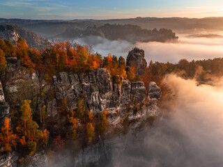 Saxon, Germany - Aerial view of the Bastei on a foggy autumn morning with colorful autumn foliage and heavy fog under the rock. Bastei is a rock formation in Saxon Switzerland National Park