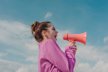 Young woman screaming through megaphone under sky