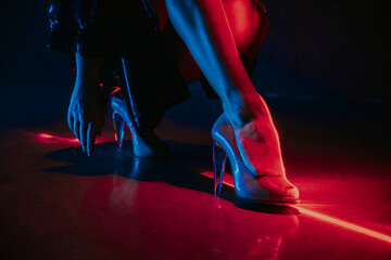 Legs of gorgeous woman in high heels shoes under red illumination, laser light, neon club....