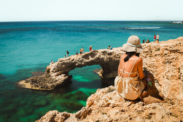 Woman tourist sit on viewpoint sightseeing Cyprus greek island visit stone arch or bridge of Love....