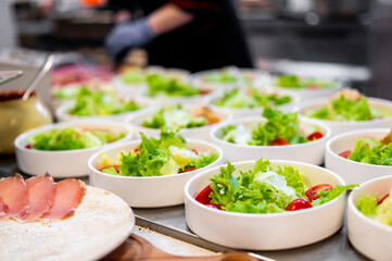 Fresh salads with vibrant green lettuce and cherry tomatoes being prepared in a professional kitchen.