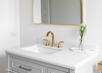 A gold bathroom faucet detail with a plant on the white marble countertop and a gold mirror.
